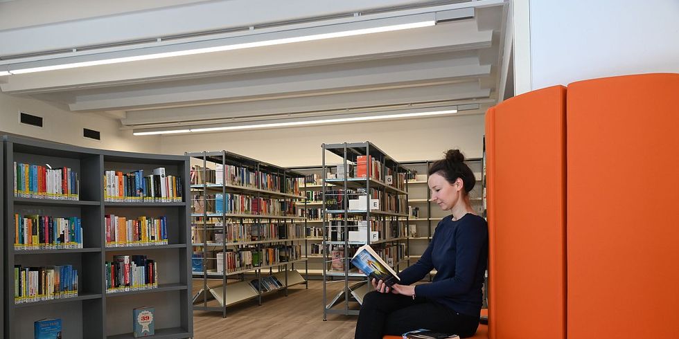Das Foto zeigt die Leiterin der Bibliothek Maria Galey in der Bibliothek auf einem roten Sofa sitzend.