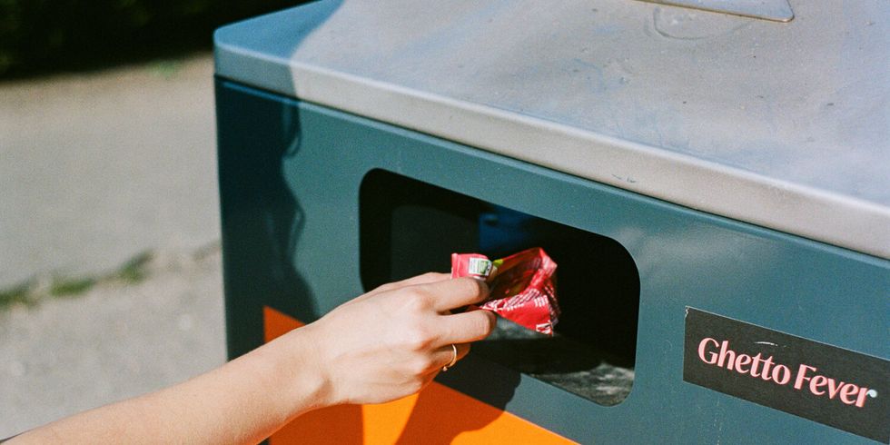 Die Hand einer Person wirft Müll in einen Mülleimer auf der Straße.