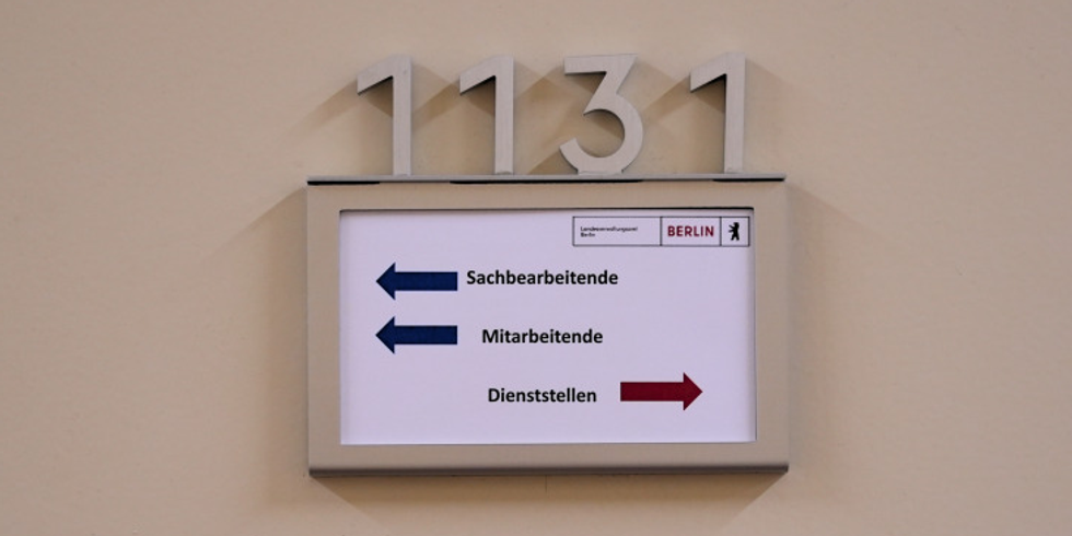 Ein Schild mit abgehenden Pfeilen von Sachbearbeitende, Mitarbeitende und Dienststellen an einer Tür