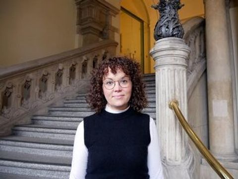 Eine Frau steht in einem Foyer vor einer Treppe.