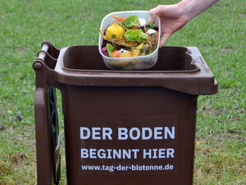 Biomüll wird in eine Biotonne mit der Aufschrift „Der Boden beginnt hier“ entsorgt