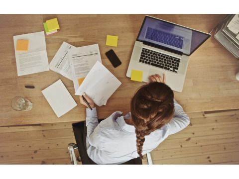 Frau arbeitend an ihrem Schreibtisch mit Dokumenten und Laptop