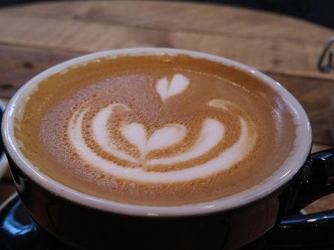 Nahaufnahme einer Tasse Kaffee mit kunstvoller Latte Art in Form von Herzen, serviert in einer schwarzen Tasse auf einem Holztisch.
