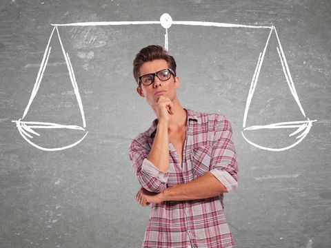 Mann steht vor Schultafel, auf der eine Waage abgebildet ist.