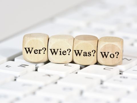 Auf einer Tastatur liegen vier Würfel mit den Aufschriften 'Wer?', 'Wie?', 'Was?', 'Wo?'