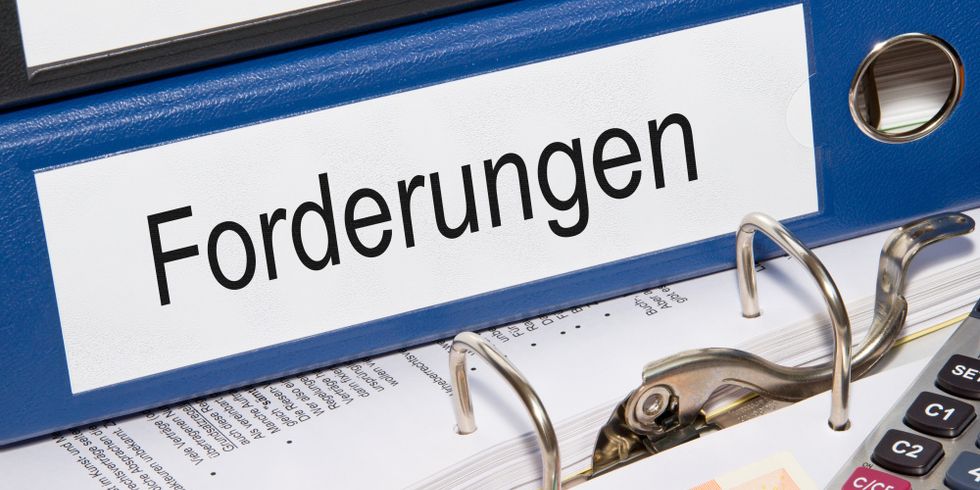 Auf einem geöffneten Aktenordner liegen ein Taschenrechner, ein Stift, mehrere Geldscheine und weitere Ordner mit der Aufschrift 'Forderungen'