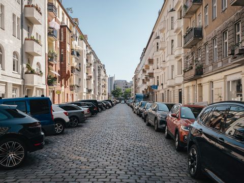 Kopfsteinpflasterstraße mit beidseitig parkenden Autos, umgeben von mehrstöckigen Wohnhäusern ohne sichtbare Grünflächen