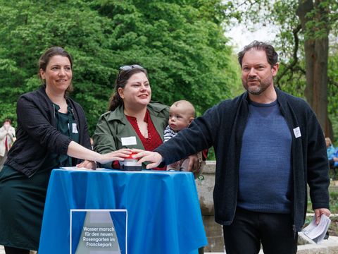 Drei Personen drücken auf einen roten Knopf im Rosengarten