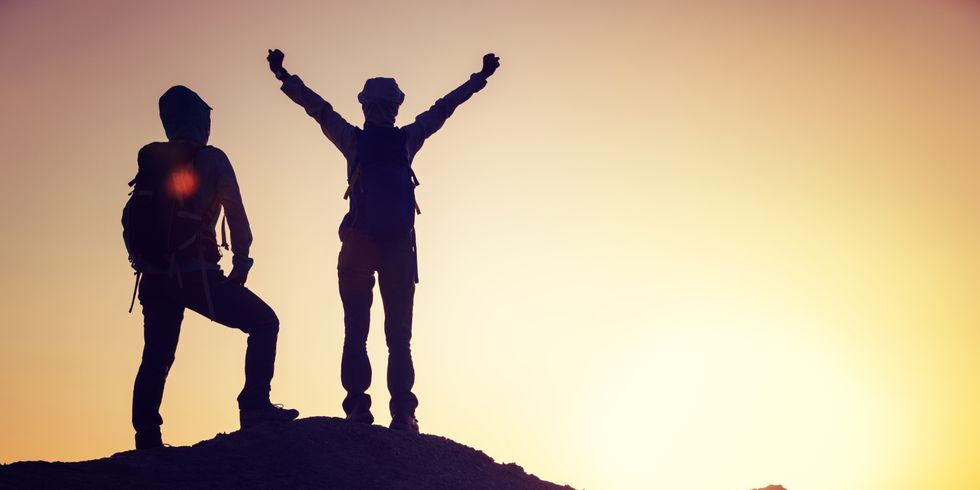 Zwei Personen stehen vor dem Sonnenaufgang auf einer Anhöhe und Freuen sich über einen Erfolg.