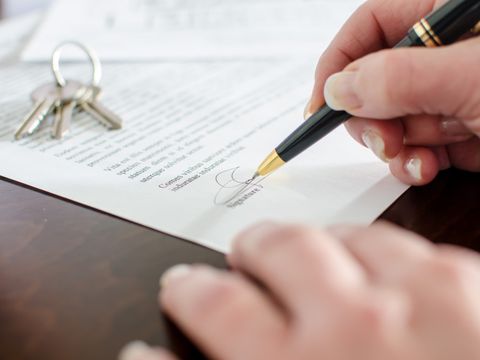 Eine Person unterschreibt ein Schriftstück, auf dem Blatt Papier liegt ein kleines Schlüsselbund