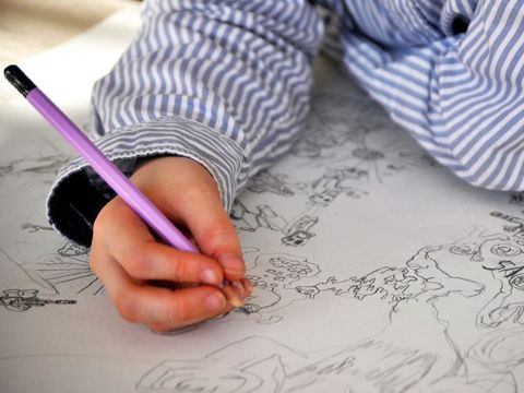 Malen & Zeichnen: Ein Kind zeichnet mit Bleistift auf Papier.