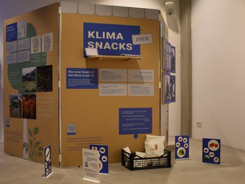Ausstellungswand mit drei Seiten, viele Bilder und Textfelder, zu lesen ist die größte Aufschrift "Klima Snacks"