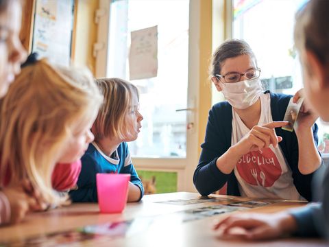 Kinder mit einer Erzieherin sitzen an einem Tisch