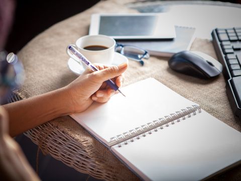 Hand, die am Tisch schreibt mit Tastatur, Maus, Tablet, Kaffeetasse