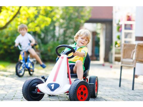 Kleines Kind Junge Tretauto im Sommergarten fahren