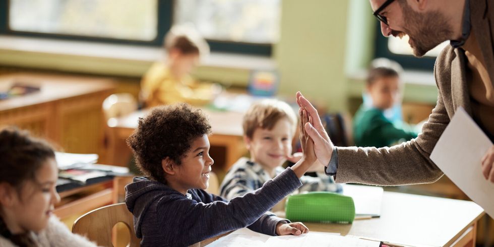 Happy teacher and schoolboy giving each other high-five on a class.