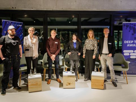 Die Panelist:innen und die Moderatorin stehen vor einer Glaswand