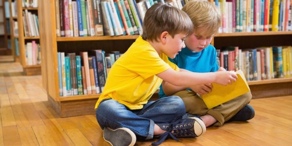 zwei Jungs sitzen vor einem Bücherregal und lesen in einem Buch