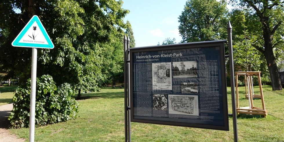 Vor einer Grünfläche steht ein Informationsschild zum Heinrich-von-Kleist-Park.