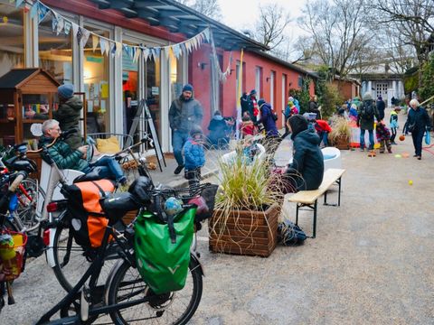 Auf einem Hof sitzen, stehen, spielen und unterhalten sich Menschen.