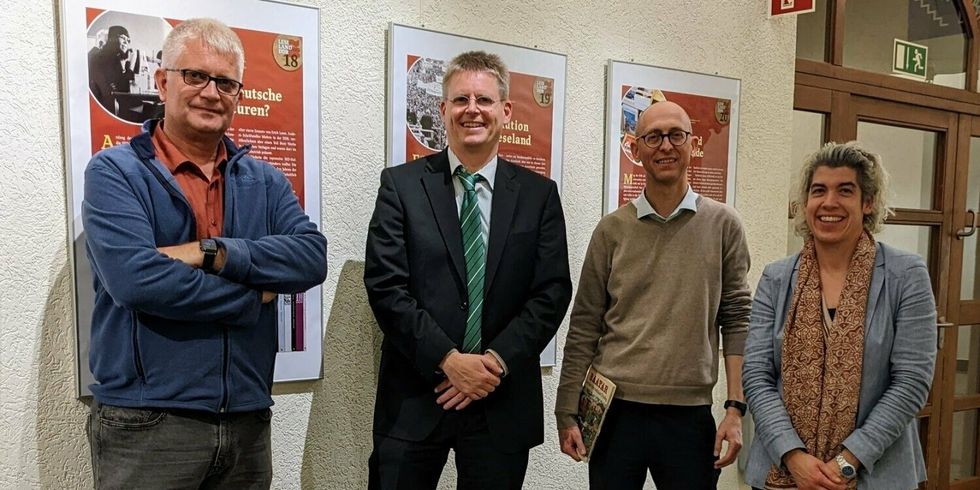 Vier Menschen stehen in einem Gang vor aufgehängten Plakaten.