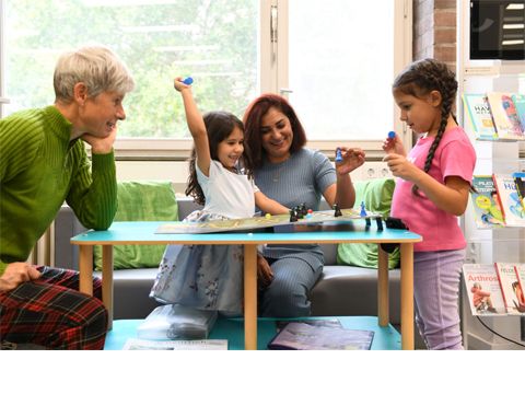Zwei Frauen mit zwei Kindern sitzen an einem Tisch und spielen ein Brettspiel