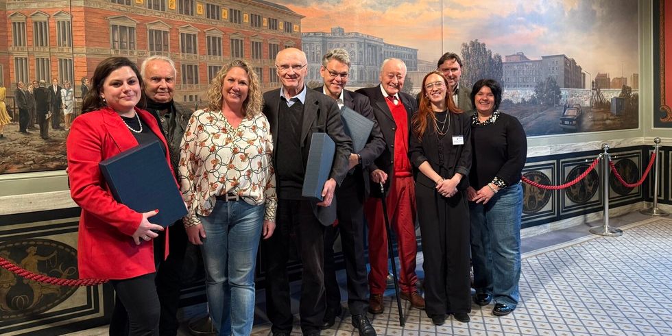9 Personen stehen zusammen vor einem Wandgemälde und lächeln.