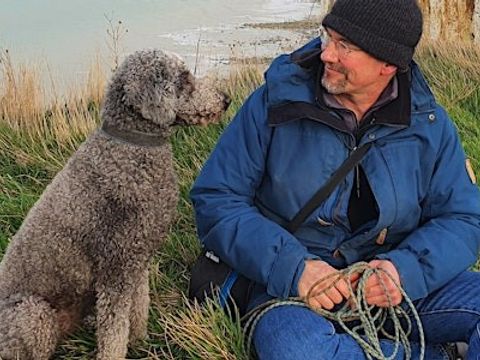 Man sitzt neben einem Hund auf einer Wiese