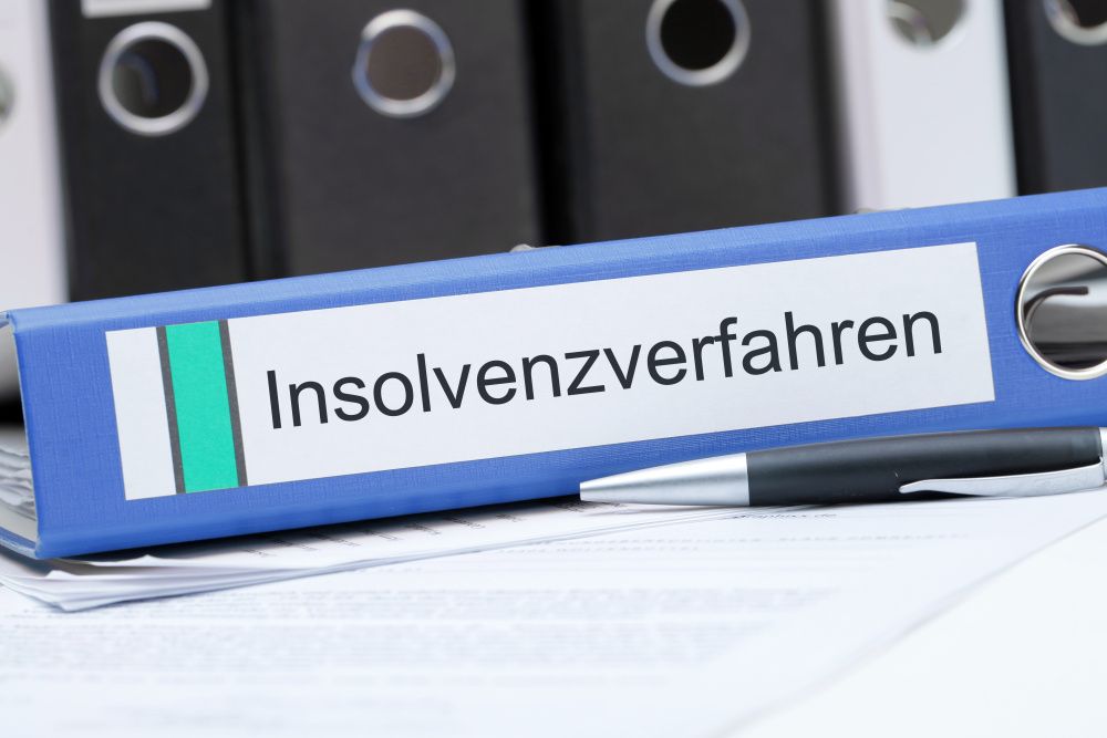 Ein Stift und ein Aktenordner mit der Aufschrift 'Insolvenzverfahren' liegen vor einer Reihe weiterer Ordner