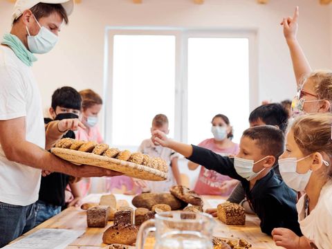 Ein Koch präsentiert Schülerinnen und Schülern Lebensmittel, die sich gegenüber an einem Tisch befinden