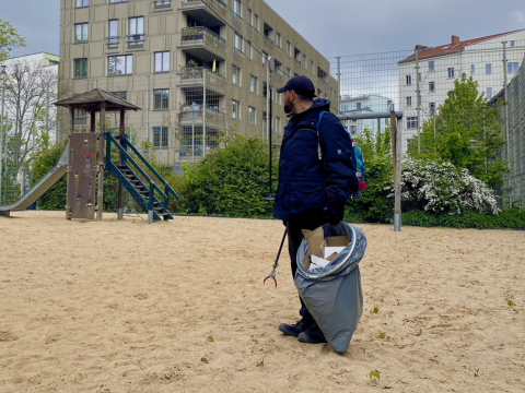 Kiezcleaner auf einem Spielplatz mit einer Mülltüte und Zange in der Hand