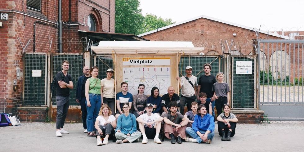 Eine Gruppe Menschen steht an einer Haltestelle auf der Vielplatz steht.
