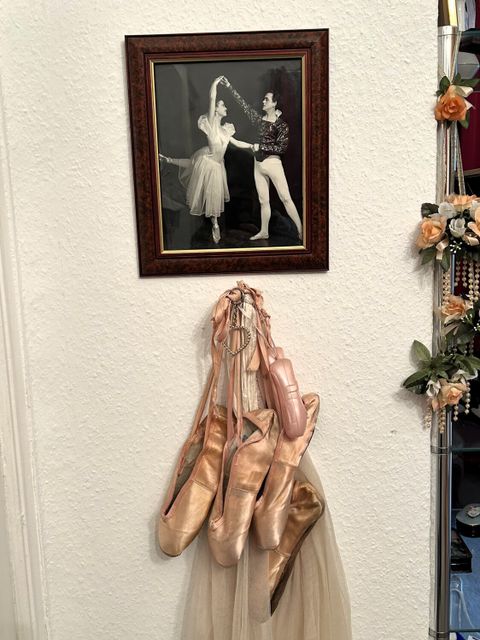Spitzenschuhe hängen unter einem Wandbild, auf dem eine Tänzerin und ein Tänzer zu sehen sind.