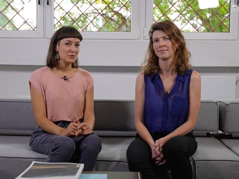 Mitgründerinnen von macht.sprache schauen frontal in die Kamera und sitzen auf einer grauen Couch