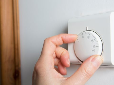 Close Up Of Female Hand On Central Heating Thermostat