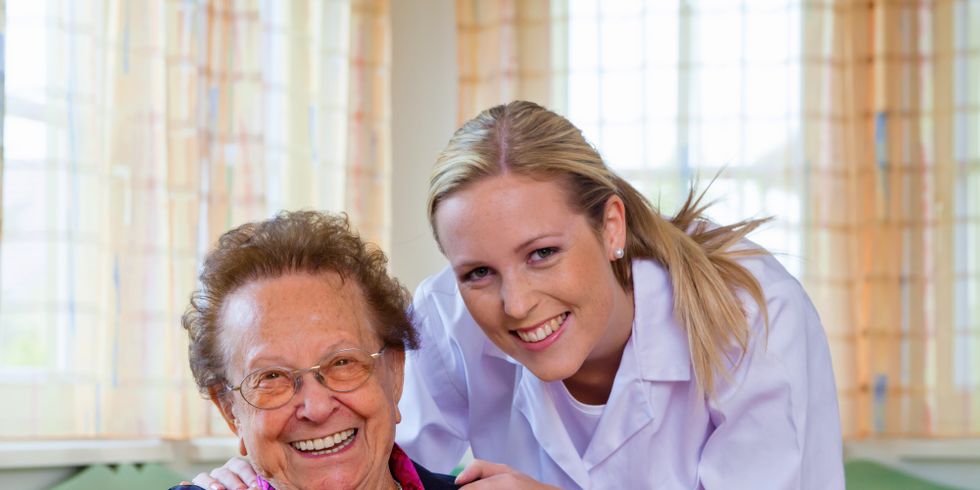 Eine Betreuerin lächelt mit einer Seniorin in die Kamera