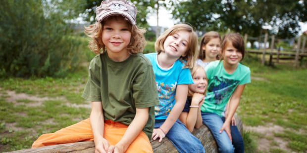 Das Bild zeigt fünf Kinder die auf einem Baumstamm sitzen