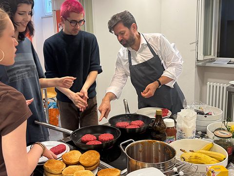 Kochkurs-Szene mit Jugendlichen und Kursleiter Michael Adrians: Das Braten von Burgerfleisch wird erklärt