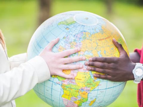 Zwei Personen halten einen Globus auf einer Wiese im Freien.