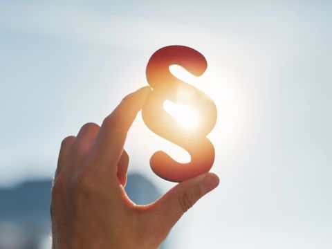 Hand hält Paragraphen Symbol in Sonne