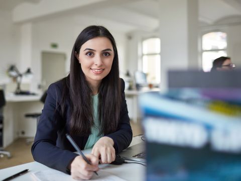 Porträt einer lächelnden Geschäftsfrau, die schreibt, während sie am Schreibtisch im Kreativbüro sitzt