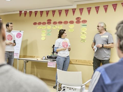 Eine Frau im Gespräch mit einem Mann, andere Personen stehen dabei und hören zu