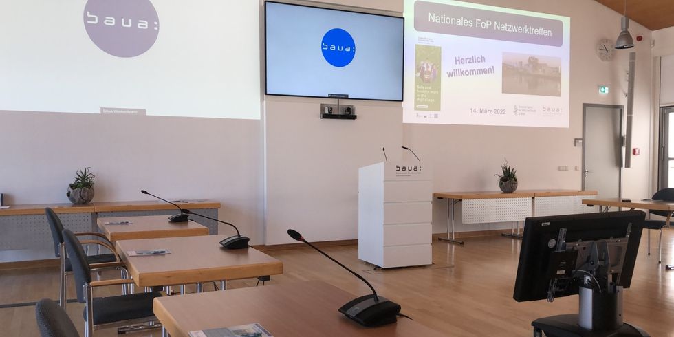 Foto vom Veranstaltungstag des nationalen Focal Point (FoP) der EU-OSHA mit Stehpult, Bildschirm und Folienpräsentation