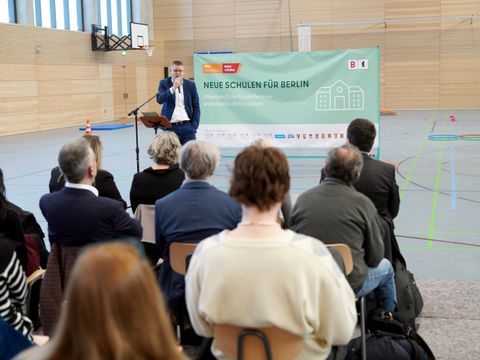 Ein Mann steht vor sitzenden Menschen in einer Turnhalle