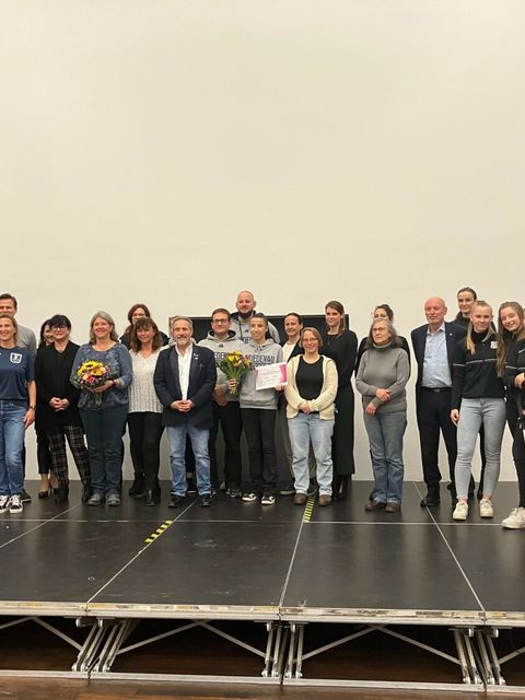 Viele Menschen stehen auf einer Bühne nebeneinander und blicken gücklich in die Kamera.