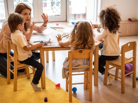 Erzieherin zählt mit kleinen Kindern am Tisch in der Kita