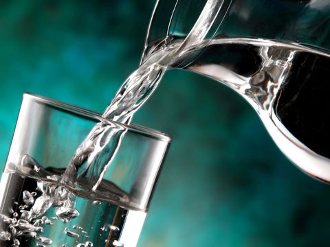 Aus einer Glaskaraffe wird ein Glas Wasser gefüllt