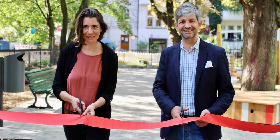 Eine Frau und ein Mann durchschneiden ein rotes Band in einem Park.