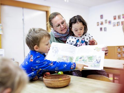 Eine Frau und drei Kinder schauen sich gemeinsam ein Bilderbuch an