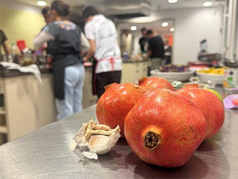 Stilleben mit Granatäfpeln. Im Hintergrund Teilnehmer:innen, die um die Kochinsel stehen.